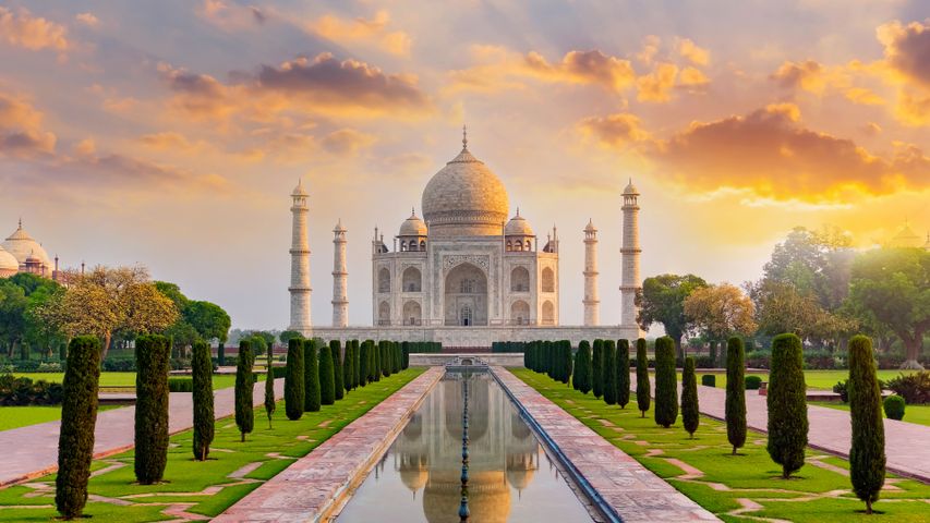 Set within the Charbagh garden, the Taj Mahal stands tall with its pristine reflection captured in the central water channel, emphasizing its architectural harmony.