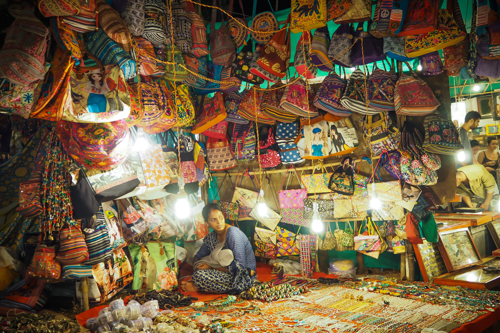 Vibrant Arpora Saturday Night Market in Goa with colorful stalls selling jewelry, food, and clothing under string lights.


