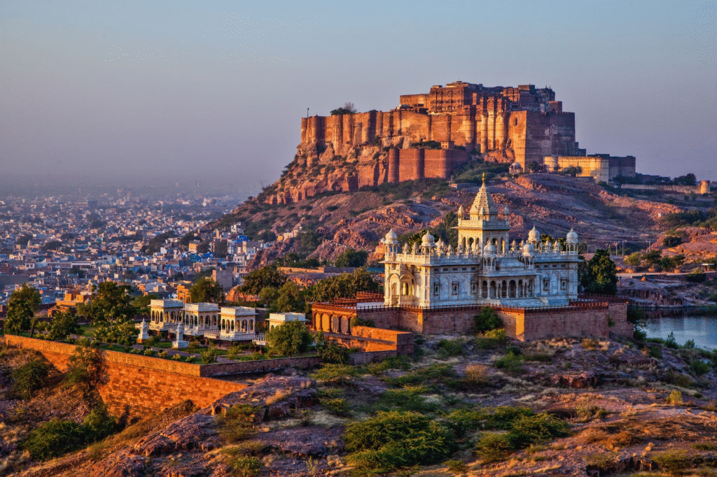 A panoramic view of Mehrangarh Fort perched atop a rocky hill, overlooking the blue city of Jodhpur under a clear sky.

