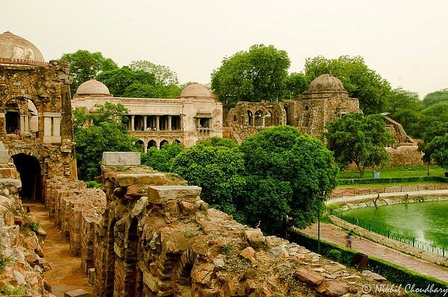 The ancient Hauz Khas Fort complex in Delhi with stone ruins overlooking a tranquil lake and lush greenery.

