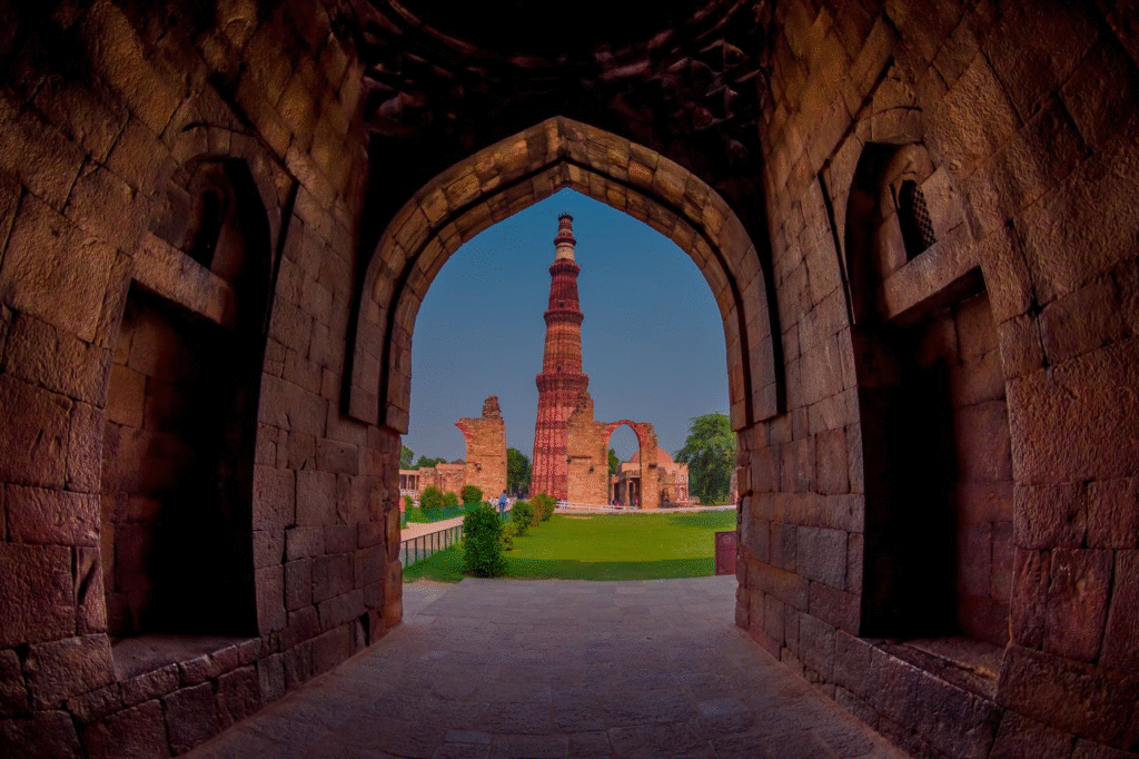 Historic Qutub Minar surrounded by ancient ruins and lush gardens on a sunny day in Delhi.