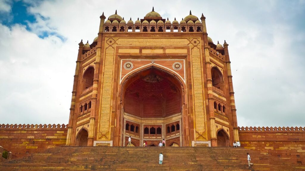 A wide-angle view of the red sandstone structures of Fatehpur Sikri, showcasing Mughal-era architecture.

