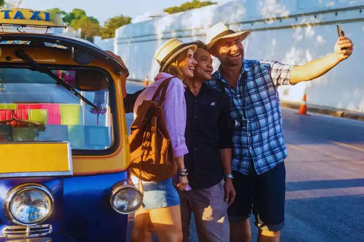 Two tourists posing for a photo with a smiling local resident in a cultural setting.