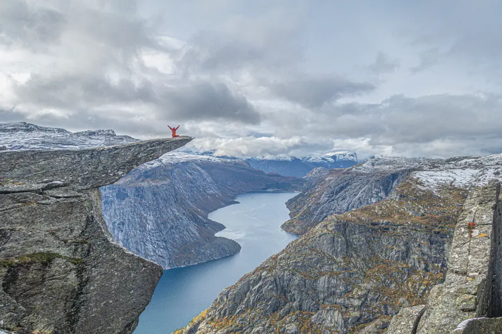 Adventurer posing on Trolltunga rock formation overlooking Lake Ringedalsvatnet in Norway
